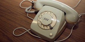 Ein altes graues Wählscheibentelefon auf einem braunen Furniertisch.