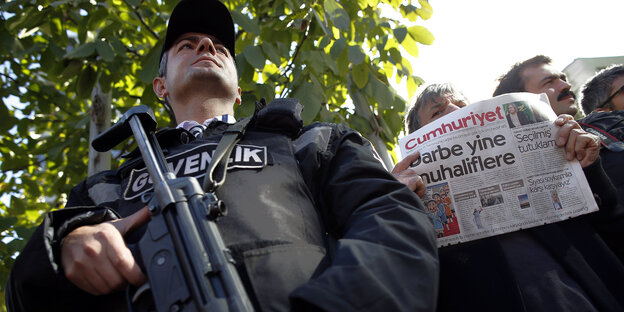 Hinter einem Polizisten mit Gewehr hält ein Mann die Cumhuriyet in die Höhe