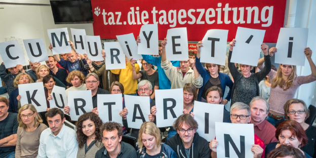 Mitarbeiter der taz halten die Buchstaben „Cumhuriyet'i Kurtarin“ in die Höhe