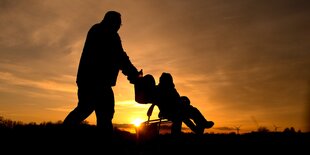 Ein Mann schiebt einen Kinderwagen. Er ist nur im Schatten vor der untergehenden Sonne zu sehen