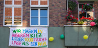 An einer grünen Hauswand hängt ein Transparent „Wir haben in unserem Kiez lieber 1000 Flüchtlinge, als 1en Nazi“. Daneben ein Balkon mit bunten Blumen