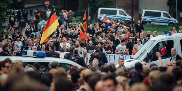 Aus einer Menschenmenge ragen Deutschlandfahnen, dahinter stehen Polizeiautos