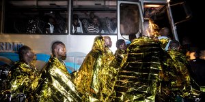 Mehrere Männer in goldfarbene Wärmefolien eingehüllt steigen bei Dunkelheit in einen Bus