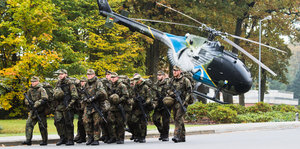 Soldaten marschieren mit Hubschrauber im Hintergrund