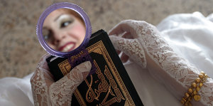 Das Gesicht einer Braut in einem Handspiegel, darunter ein Koran