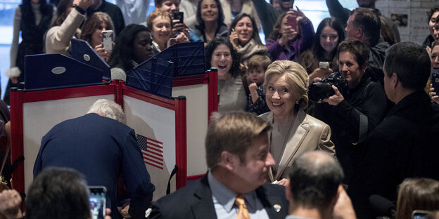 Hillary Clinton in einem Wahllokal. In der Wahlkabine steht ihr Mann Bill Clinton Hillary Clinton in einem Wahllokal. In der Wahlkabine steht ihr Mann Bill Clinton