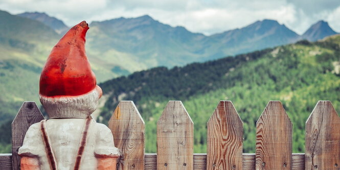 Ein Gartenzwerg steht an einem Zaun mit Blick auf Berge