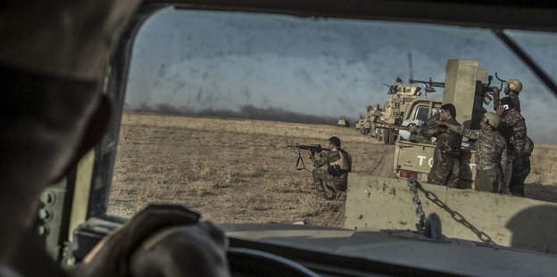 Blick durch eine Scheibe. Draußen richten Kämpfer in Tarnkleidung von einem Panzer aus Waffen in eine Richtung