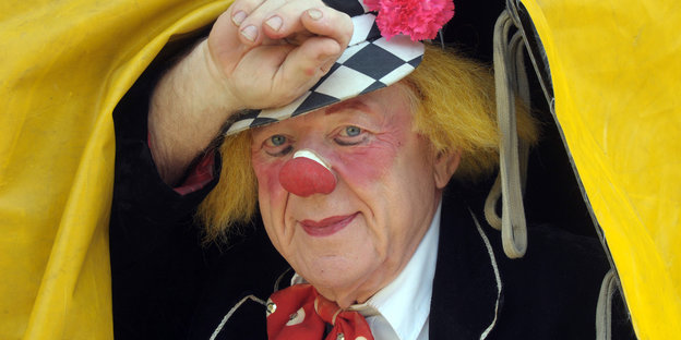 Clown mit gelben Haaren und roter Nase schaut aus dem Zelt heraus