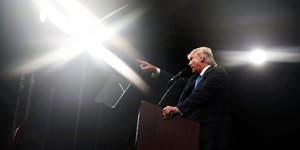 Donald Trump spricht, stützt sich mit dem linken Arm auf ein Pult und zeigt mit dem rechten nach vorne
