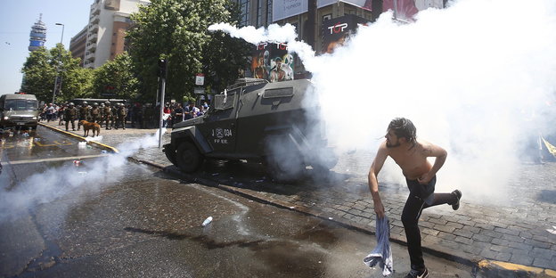 Ein Mann vor einem gepanzerten Fahrzeug in Tränengasschwaden