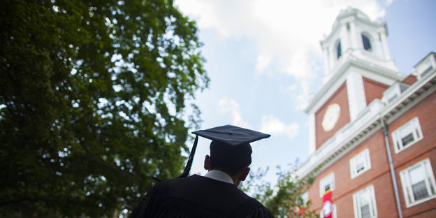 Rückenansicht eines Studierenden mit Robe und Graduierten-Kopfbedeckung auf dem Campus Harvard