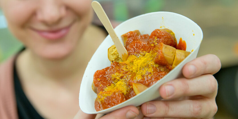 Eine junge Frau hält eine Pappschale mit Currywurst