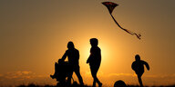 Ein Paar mit Kinderwagen und Kind steht vor einer untergehenden Sonne, ein Drachen steigt auf