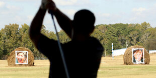 Ein Golfspieler zielt auf zwei Strohballen mit dem Konterfei von Clinton und Trump