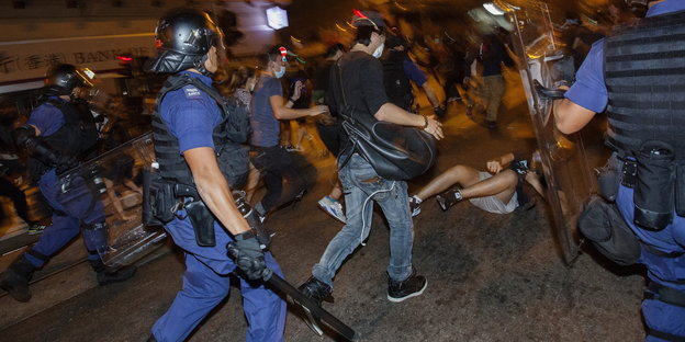 Es ist Abend oder Nacht: Polizisten mit Helmen und Schlagstöcken gegen andere Menschen