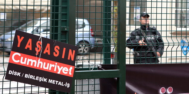 Ein Schild mit der Aufschrift "Lang lebe Cumhuriyet" befindet sich am Zaun der Zeitungsredaktion hinter dem ein bewaffneter Polizist Wache steht
