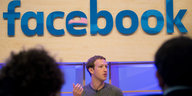 Ein junger Mann in grauem Tshirt sitzt unter einem Schild mit der Aufschrift "facebook"