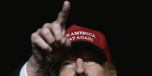 Donald Trump trägt eine rote Baseball-Kappe und streckt den Zeigefinger in die Luft