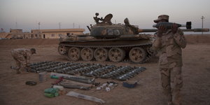Zwei Soldaten sortieren vor einem Panzer Bomben und Waffen