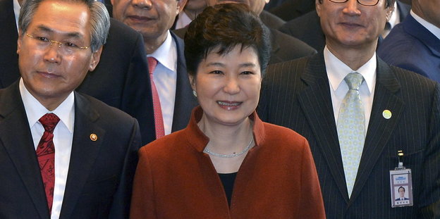 Die koreanische Präsidentin in roter Jacke inmitten von Männern in Anzügen