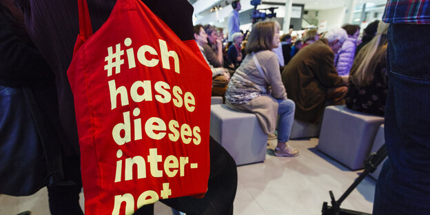 Tasche mit Aufschrift: „Ich hasse dieses Internet“ - auf der Buchmesse, im Hintergrund sitzende Personen bei einer Veranstaltung