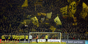 Ein Fußballteam in gelben Trickots steht vor der Fankurve eines Stadions, auf der gelbe Fahnen geschwenkt werden