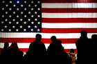 Die schwarzen Silhouetten mehrerer Menschen vor einer großen US-Flagge
