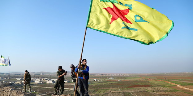 Kurdische Kämpfer halten eine YPG-Fahne hoch