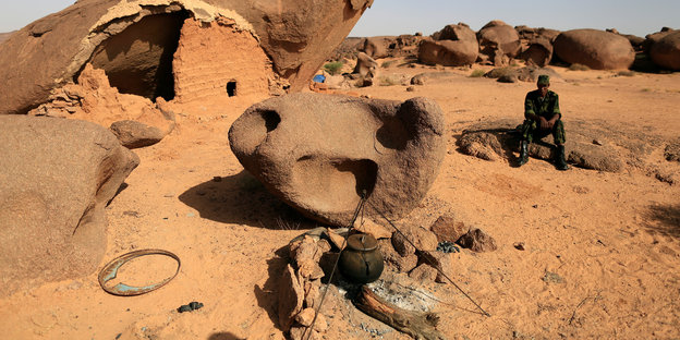 Ein Polisario-Kämpfer hockt auf einem Stein in der Wüste. Im Vordergrund eine Feuerstelle
