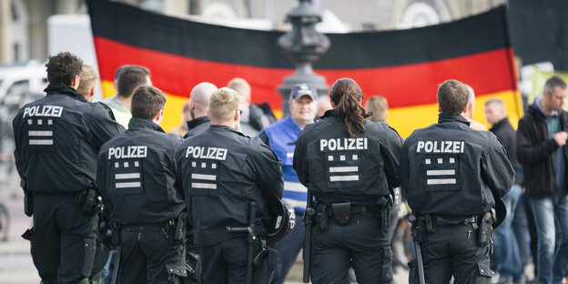 PolizistInnen vor DemonstrantInnen mit einer großen Deutschlandflagge