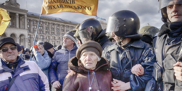 Demonstranten und Polizisten auf einer Straße in Kiew. Ganz vorne eine entrüstete Rentnerin