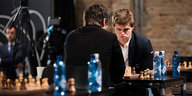 Magnus Carlsen sitzt einem Kontrahenten gegenüber und blickt auf das Schachfeld