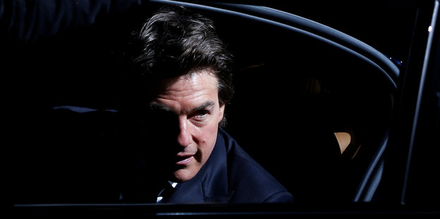 Tom Cruise steigt aus einem dunklen Auto, die Hälfte seines Gesichts liegt in Schatten