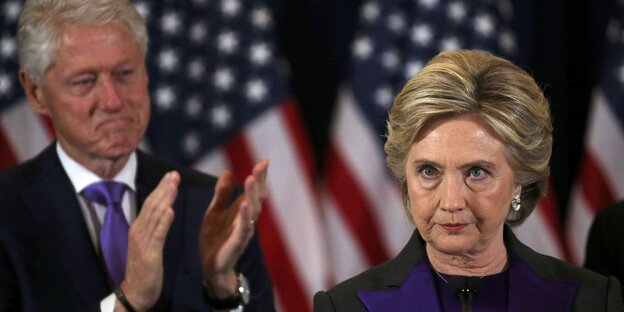 Hillary Clinton blickt streng, Bill Clinton applaudiert