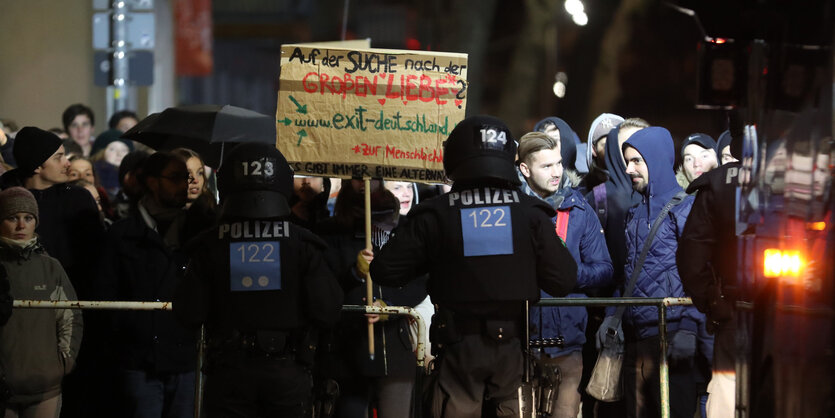 Menschen mit Plakaten stehen vor einer Polizeiabsperrung