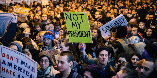 Eine Menschenmasse, in der Einzelne Schilder hochhalten, auf denen zum Beispiel "Not my president" geschrieben ist