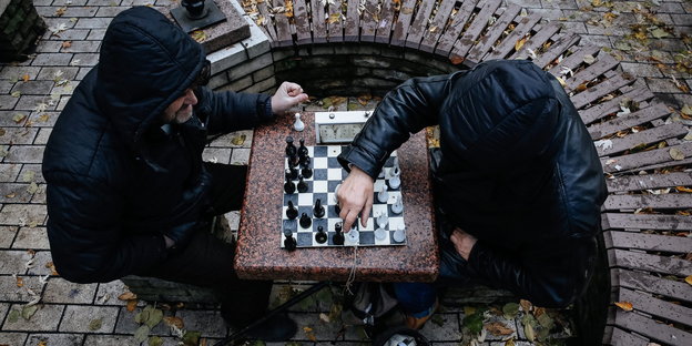 Foto von oben auf zwei Männer in Kapuzenjacken, die an einem Betontisch Schach spielen