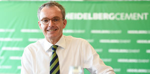 Ein Mann in Hemd und gestreifter Krawatte steht vor einem grünen Hintergrund