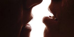 Die Silhouetten zweier sich küssender Münder vor einem weißen Hintergrund
