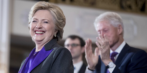 Die demokratische US-Präsidentschaftskandidatin Hillary Clinton steht lachend an einem Rednerpult, hinter ihr klatscht ihr Ehemann Bill Clinton