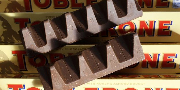 Auf mehreren Toblerone-Schachteln liegen zwei Schokoriegel - einmal mit der normalen Anzahl an Dreiecken, einmal in der reduzierten Variante.
