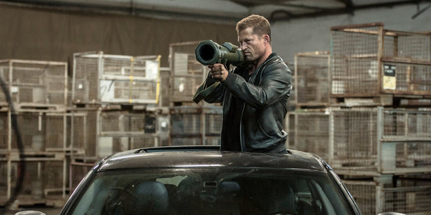 Schauspieler Til Schweiger schaut im "Tatort" mit einer Bazooka aus dem Dachfenster eines Autos heraus