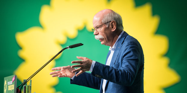 ein Mann spricht vor einem großen Grünen-Logo in ein Mikrofon