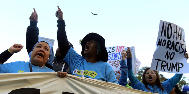 Mehrere Frauen hinter einem Transparent skandieren Slogans und zeigen mit dem Arm in die Luft