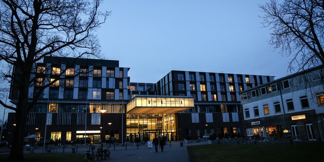 ein hellerleuchtetes Klinikgebäude in der Abenddämmerung