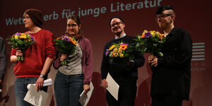 Mit Blumensträußen stehen vier junge Manner und Frauen aunf einem Podium.