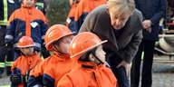 Bundeskanzlerin Angela Merkel beugt sich zu mehreren Kindern in Feuerwehruniformen herunter