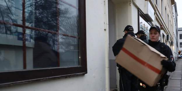 Polizisten tragen Kartons aus einem Haus