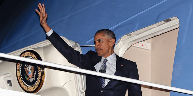 Barack Obama steht im EIngang seines Flugzeugs und hebt die Hand zum Gruß